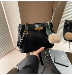 Detail of black leather handbag with gold buckle and plush green leaf charm accessory