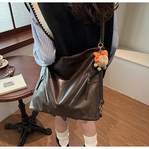 Detail of dark brown tote bag with zipper pockets and a plush pendant accessory