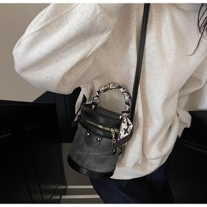 Detail of grey bucket bag with silk scarf handle and gold zipper in a minimalist setting