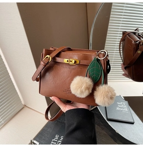 Detail of brown leather handbag featuring gold twist lock and cherry fur ball charm