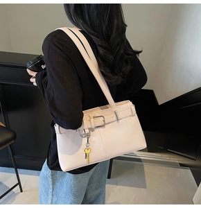 Detail view of the beige minimalist hobo bag with a gold key pendant and shoulder strap