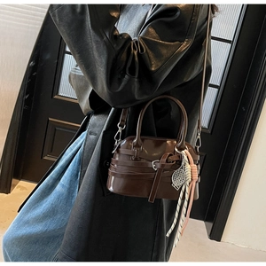 Detail of dark brown leather shoulder bag with buckle straps and tennis racket pendant