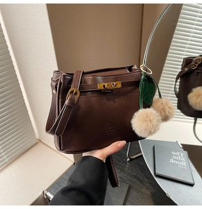 Detail of dark brown leather handbag featuring a gold twist lock and cherry fur charm