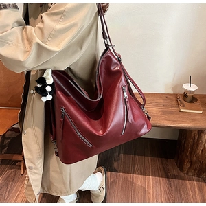 Detail of burgundy leather tote bag with silver zippers and a cute panda plush charm