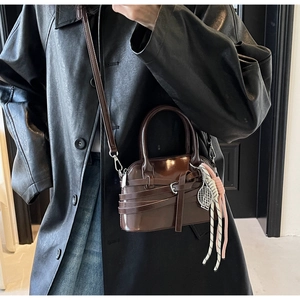 Detail of dark brown leather shell bag with unique wrap strap and tennis racket charm