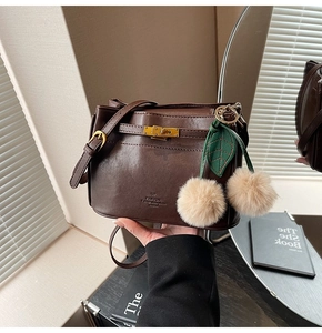 Detail of dark brown leather handbag with gold twist lock and cherry fur pompom charm