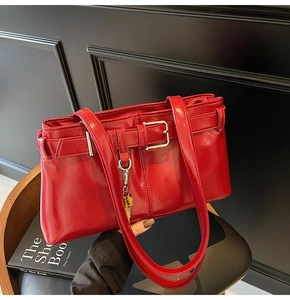 Detail of red glossy leather shoulder bag with vintage buckles on dark wooden background