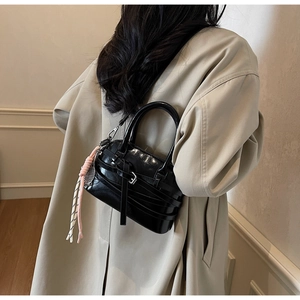 Detail of black glossy handbag with pink woven cord shown on model in beige coat