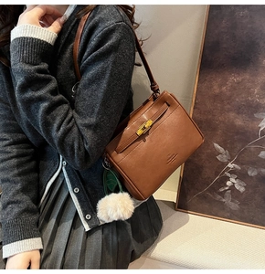 Detailed view of a brown leather crossbody bag featuring a gold twist lock and fur ball charm
