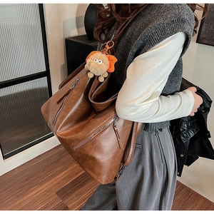 Detail of vintage brown PU leather shoulder bag featuring metal zippers and plush charm