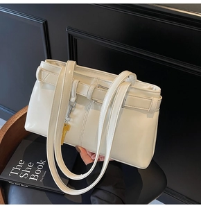 Detail of a creamy white tote bag featuring a leather buckle and a gold key charm