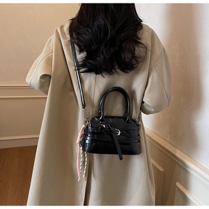 Detail of black glossy patent leather shoulder bag with buckle strap and woven pendant