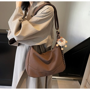 Detail of a deep brown half-moon crossbody bag with a plush lion charm on a trench coat