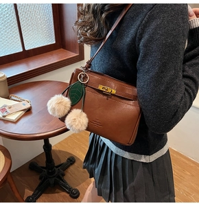 Detail of dark brown leather handbag with gold metal lock and plush cherry charm