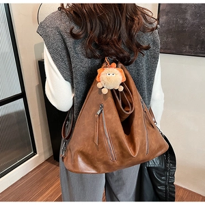 Brown vintage leather shoulder bag with lion plush pendant and multiple zipper pockets