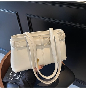 Detail of cream white leather shoulder bag featuring belt buckle straps and gold key charm