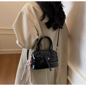 Detail of black glossy handbag with decorative buckle and colorful woven charm pendant