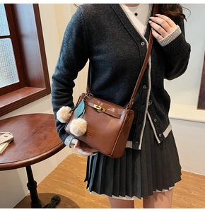 Brown leather crossbody bag with gold buckle and pom-pom detail shown on a model