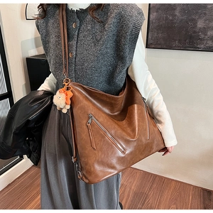 Close-up of vintage brown PU leather hobo bag with plush charm and metal zippers