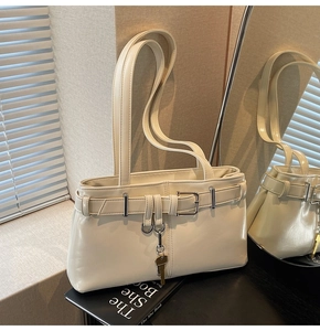 Detail of cream patent leather shoulder bag with buckle and key charm on a book