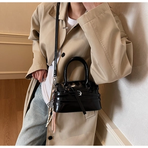 Detail of glossy black handbag featuring silver buckles and a pink tassel charm