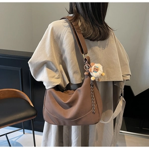 Brown dumpling cross-body bag with wide shoulder strap and plush lion pendant detail