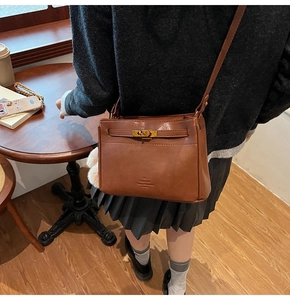 Close-up of a vintage brown leather bag with a golden metal turn-lock and fine texture