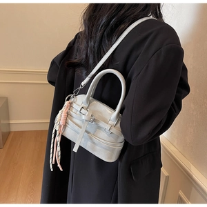 Detail of silver shell shoulder bag featuring crisscross straps and colorful tassel charm