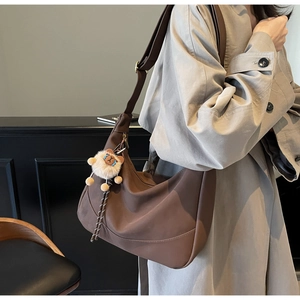 Detail of dark brown hobo bag with wide shoulder strap and white alpaca plush charm
