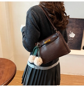 Detail of dark brown leather underarm bag with gold lock and plush pompom charm decoration