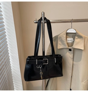 Close-up of black glossy patent leather shoulder bag with metallic key charm detail