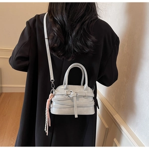 Detail of light gray shell shoulder bag with decorative cross straps and fringe tassel