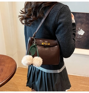 Detail of dark brown leather underarm bag featuring a cherry charm and gold twist lock