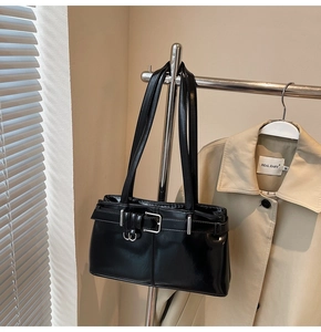 Detail of black patent leather shoulder bag with silver buckles hanging on a display