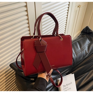 Details der burgunderroten Ledertasche mit Schleife, Goldlogo und langem Schultergurt
