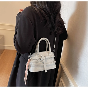 Detail of light grey shell-shaped handbag with leather strap wraps and tassel accessory