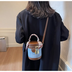 Detail of denim cylinder bag with brown leather trim and scarf-wrapped handle