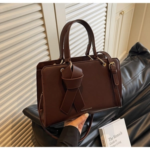 Detail einer dunkelbraunen Ledertasche mit elegantem Knotendesign und Goldbeschlägen