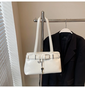 Detail of white leather shoulder bag featuring silver buckle straps and a key pendant