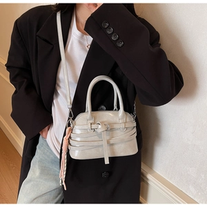 Close-up of light gray shell bag with decorative wrap straps and pink tassel detail