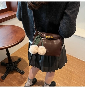 Detail of dark brown handbag featuring a gold twist lock and cherry plush charm