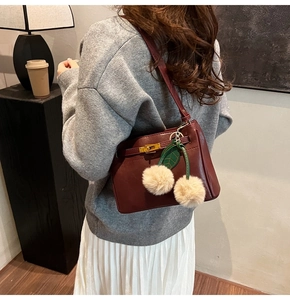 Detail of burgundy leather shoulder bag with gold clasp and plush cherry charm decoration
