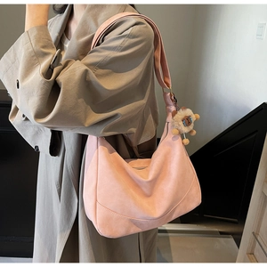 Close-up of light pink crescent bag with plush lion charm and suede texture