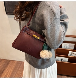Detail of burgundy handbag showing golden hardware lock and plush charm on PU leather