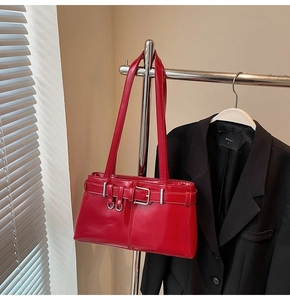 Close-up of red patent leather shoulder bag with decorative straps and metal buckles