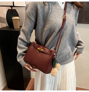 Detail of burgundy crossbody bag featuring gold hardware and a decorative plush charm