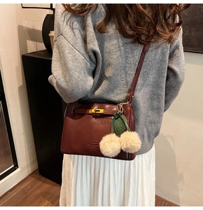 Detail of dark red leather shoulder bag with gold twist lock and cherry bag charm