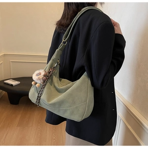 Detail of olive green suede crescent bag with plush charm and woven strap on model