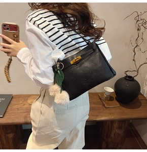 Detail view of a black leather handbag with gold twist lock and plush charm on a model