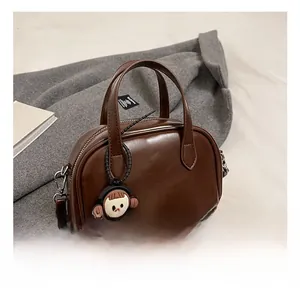 Detailansicht einer dunkelbraunen Boston-Handtasche mit Griffen und Puppenanhänger